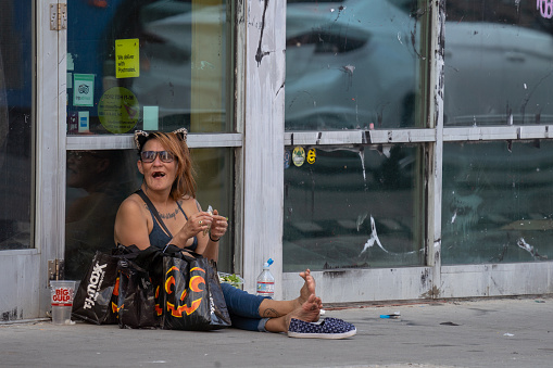 Denver, September 2022:  A woman homeless of Denver city on the street sit on the street in hot day.