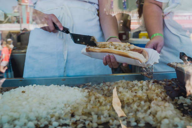istock Worker scoops grilled onions onto a footlong hotdog while working in a booth at a fair 1421733415