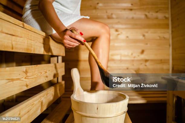 Hand Of Unknown Caucasian Woman In Sauna Spa Taking Water From Bucket With Wooden Spoon To Pour On The Hot Stones Stock Photo - Download Image Now