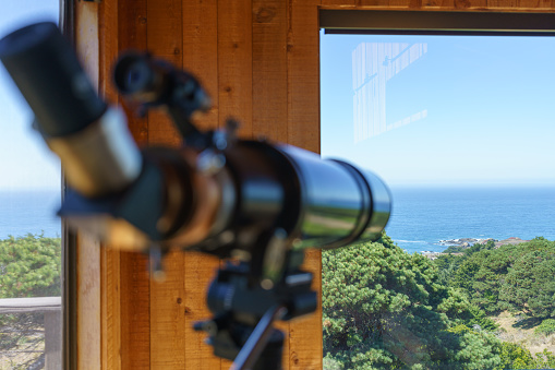 Telescope in home by windows looking toward ocean