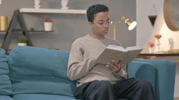 istock African Woman Reading Book while Sitting in Sofa 1421739437