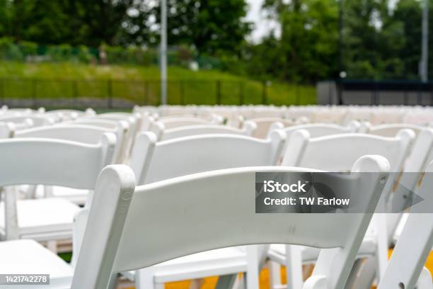 White Chairs Setup In Rows On A Green Synthetic Turf Athletic Field For A High School Graduation Ceremony Stock Photo - Download Image Now