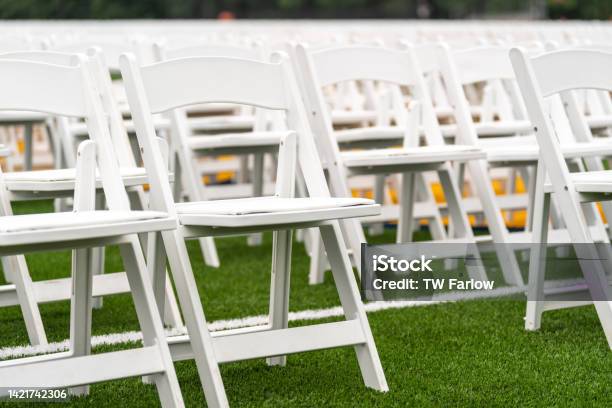 White Chairs Setup In Rows On A Green Synthetic Turf Athletic Field For A High School Graduation Ceremony Stock Photo - Download Image Now