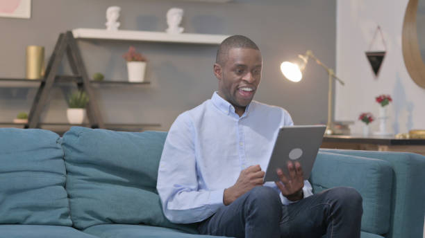 istock African Man Celebrating Success on Tablet on Sofa 1421756332