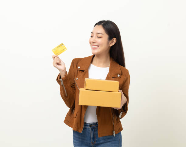 istock Young beautiful asian woman with parcel cardboard standing on isolated white background. Delivery woman holding credit card shopping online. 1421756521