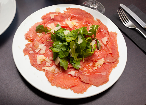 Carpaccio and cheese served on plate with arugula sprigs. Dish made of raw beef meat.