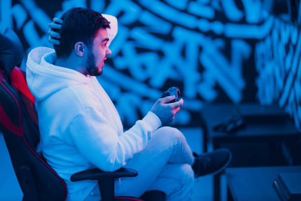 istock Young man plays on game console with gamepad sitting on chair 1421771339