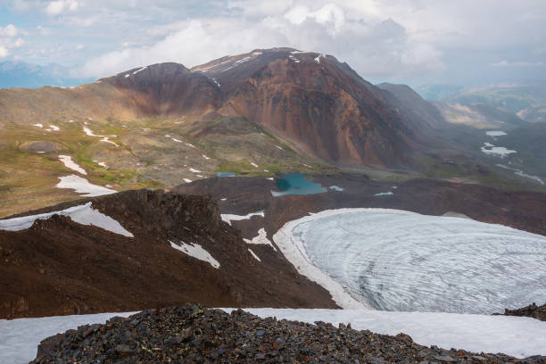 Dramatic landscape with contrast between sunny and rainy weather. Awesome scenery with sharp rocks and small lake in mountain valley. Changeable weather in mountains is sunny and cloudy at same time.