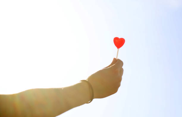 istock Hand holding a bright red love heart lollypop 1421776133