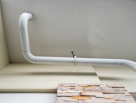 The white curve pipe for drainage of the air conditioner system is hanging on the ceiling of the office building,  below the view with the copy space.
