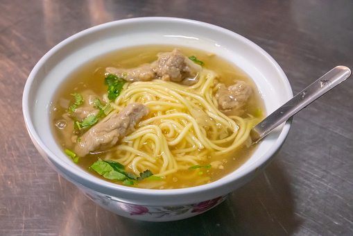 Taiwanese noodle soup, a close up of traditional homemade hot yellow noodle with pork on table at restaurant in Kaohsiung, Taiwan.