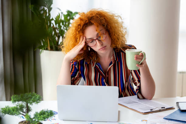 young woman tired, exhausted from working studying hard. bored and frustrated. head resting on hand. bright space big windows. at home concept. stress concept. - burning the candle at both ends imagens e fotografias de stock