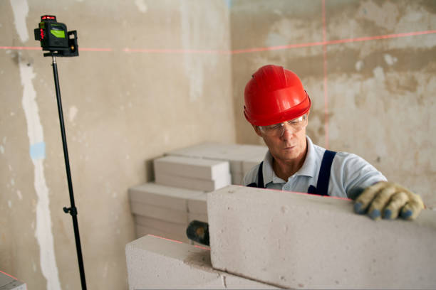 Bricklayer using rubber mallet hammer to tap, level concrete blocks wall. Contractor uses precise spirit bubble and laser level for brickwork. Worker constructs a wall in new apartment real estate. albañil que utiliza martillo de mazo de goma para golpear y nivelar la pared de bloques de hormigón. el contratista utiliza una burbuja de espíritu precisa y un nivel láser para el ladrillo. trabajador construye un muro en nuevos inmuebles de apartamen