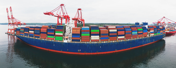 Aerial drone view of an enormous (300m) container ship at docked at port.