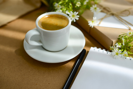 Coffee, flowers and gift box with blank card, soft focus, blurred background. Black coffee in white cup and first spring flowers on a desk. Coffee still life in Eco friendly style
