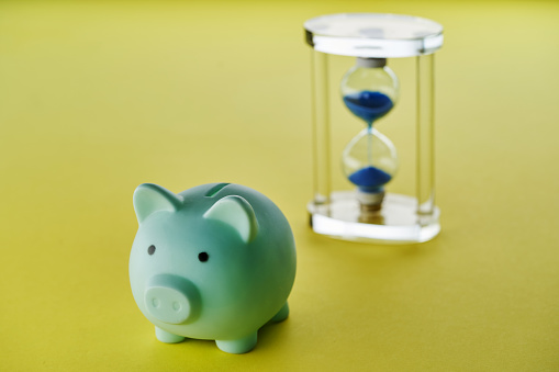 piggy bank and hour glass on yellow background