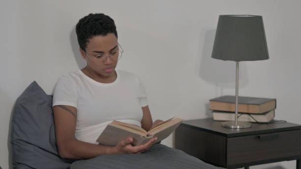 istock African Woman Reading Book while Sitting in Bed 1421790342