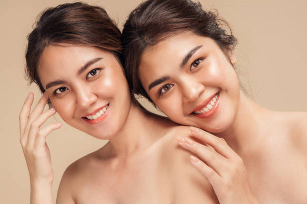 Two Asian female models happy smiling with perfect face skin and natural makeup on beige background. stock photo