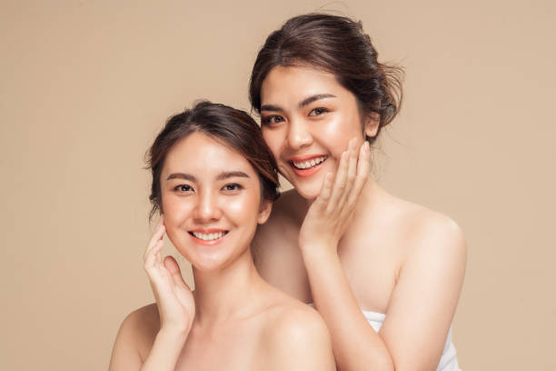 Two beautiful female models happy smiling with perfect face skin and natural makeup on beige background. Two Asian woman with beauty face touching healthy skin care. Beautiful female models happy smiling with perfect face skin and natural makeup on beige background. Spa skin care concept. asian eyebrows stock pictures, royalty-free photos & images