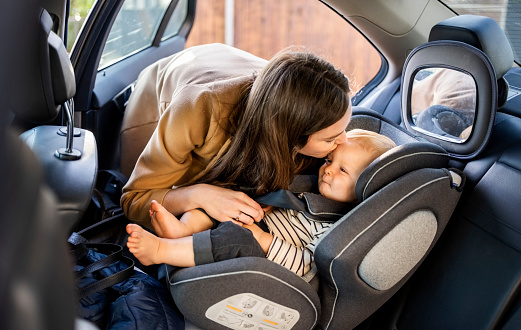 Loving mother kissing her son sitting in the safety seat of her car before going to a ride