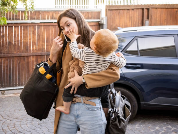 Woman carrying her son talking on mobile phone in driveway Woman carrying her son talking on mobile phone while walking in driveway with car parked at back returning home from work stock pictures, royalty-free photos & images