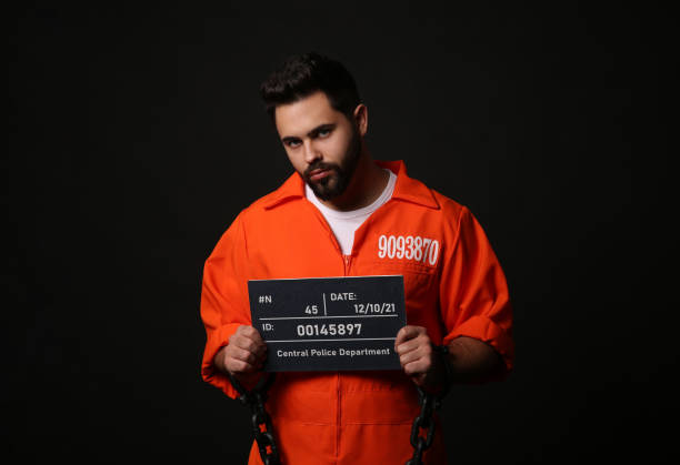 istock Prisoner with chained hands holding mugshot letter board on black background 1421800725