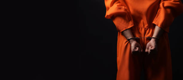 istock Prisoner in jumpsuit with handcuffs on black background, closeup. Space for text 1421800739