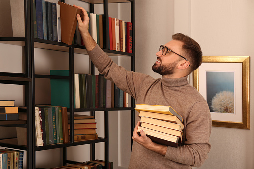 Young man choosing books on shelf in home library