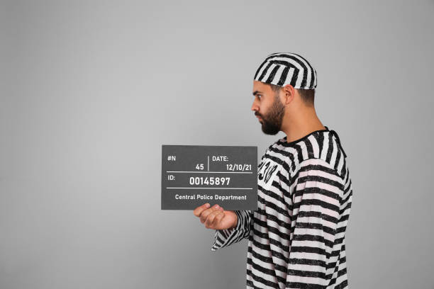 istock Prisoner in special uniform with mugshot letter board on grey background, space for text 1421804748
