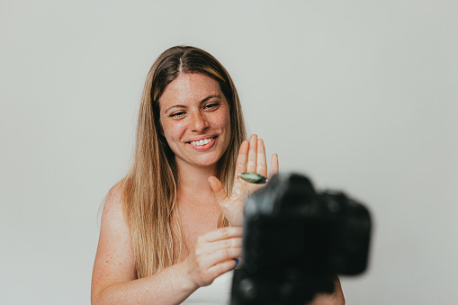 Young freckled woman filling a video using a jade roller in a studio with a white background