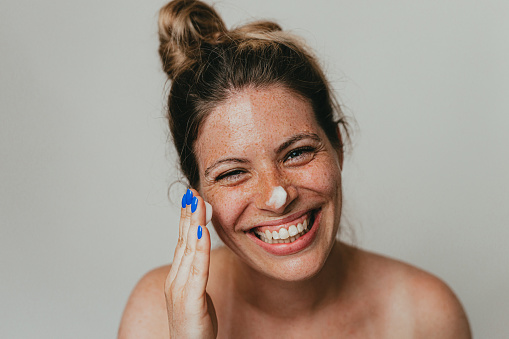 Mujer feliz con pecas aplicando crema hidratante en la cara photo