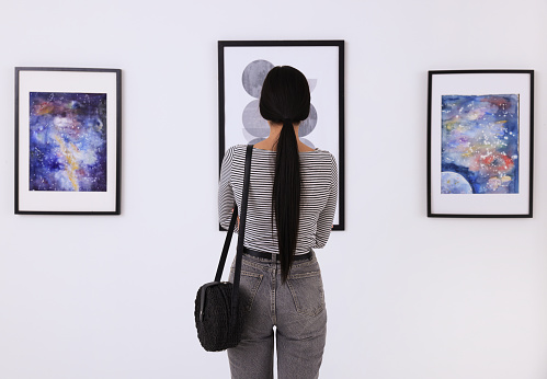 Young woman at exhibition in art gallery, back view