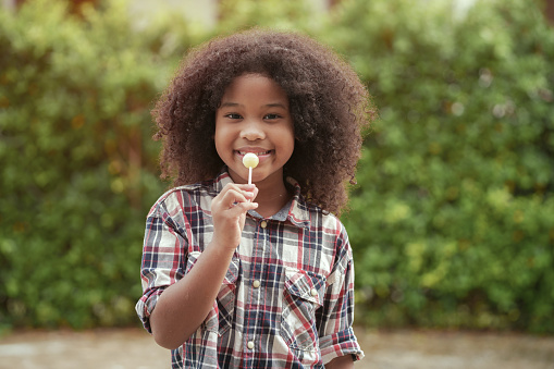 Happy African-American kid girl with a lollipop in her hands in the garden or outdoors.