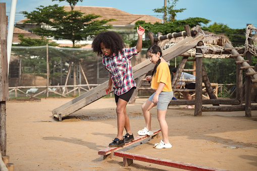Two girl kid walks on a log, keeping her balance, walking on the playground.