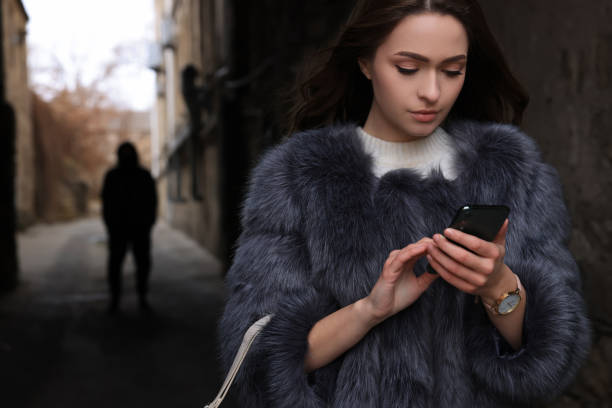 Man stalking young woman with phone in alley stock photo