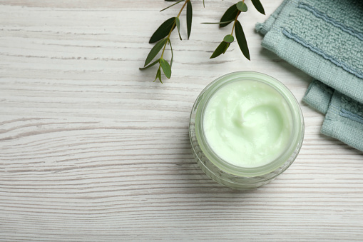 Jar of organic cream, towel and eucalyptus on white wooden table, flat lay. Space for text