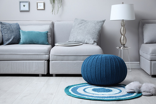 Stylish living room interior with comfortable sofa and knitted pouf