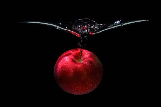 Photo of Red apple dropped in water with splashes on black