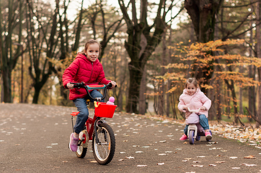 Two happy little girls riding a bike in autumn park