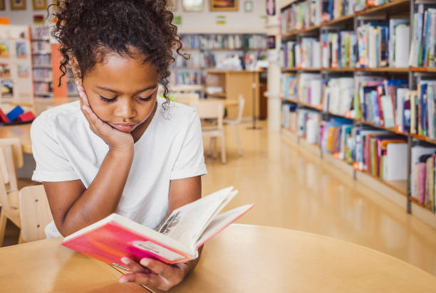 istock Young kid reading a book in the library 1421824417