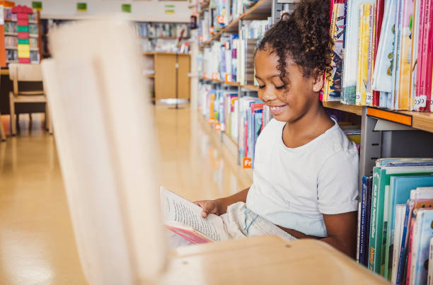 istock Young kid reading a book in the library 1421824451