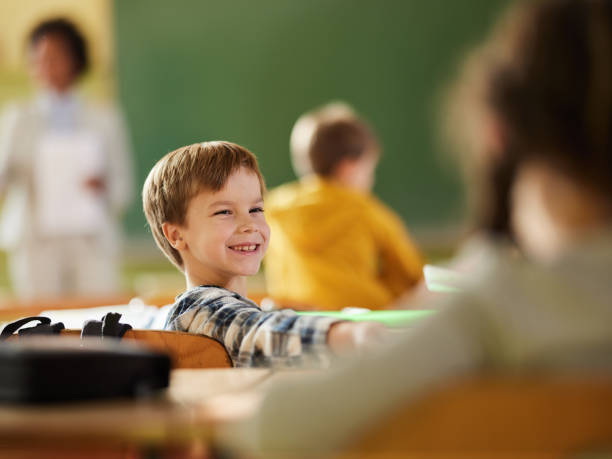 istock Happy schoolboy turning to his classmate in the classroom. 1421825967