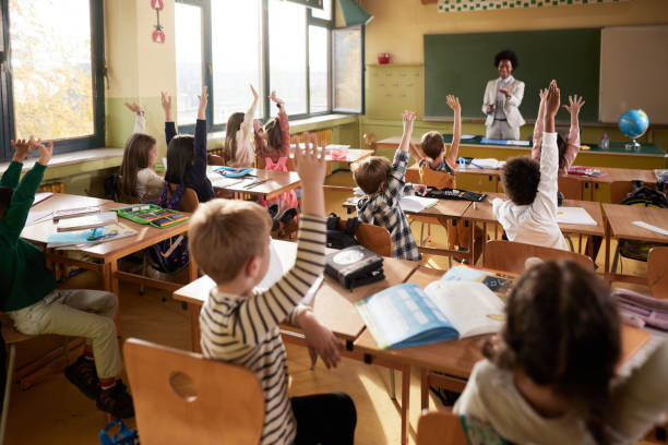 istock Back view of students raising their hands to answer the teacher's question on a class. 1421826046