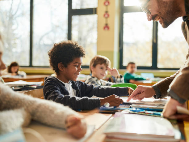 istock Happy male teacher assisting his students on a class at elementary school. 1421826240