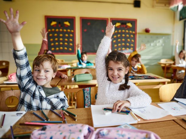 istock Happy elementary students raising their hands on a class at school. 1421826315