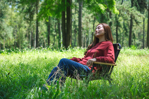 Portrait image of a beautiful young asian woman with closed eyes sitting and relaxing on a chair in the park