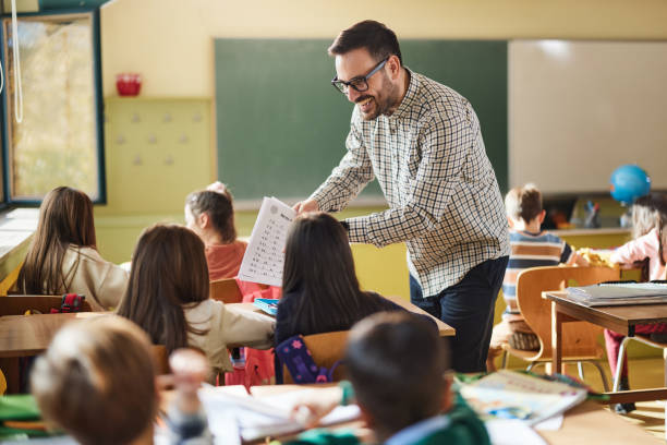 istock Happy male teacher talking to his students on a class at elementary school. 1421827119