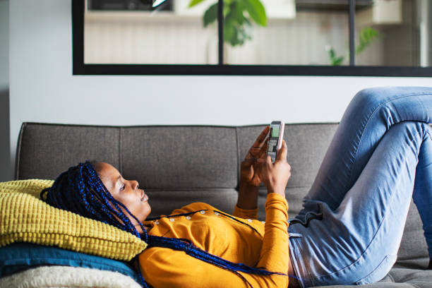 istock Young African woman lying down at sofa and using mobile at home 1421840853
