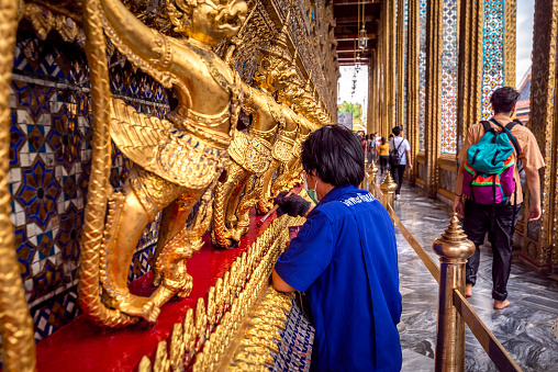 Bangkok, Thailand - September 9, 2019: man is restoring the Golden garuda and naga statue, the decoration on a wall of The Emerald Buddha temple, Wat Phra Kaew, Grand Palace, Bangkok, Thailand