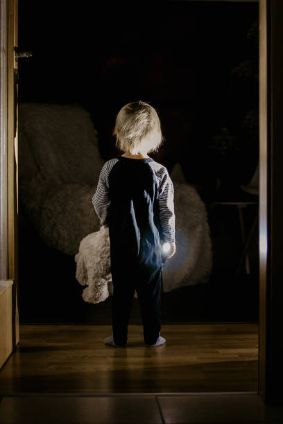 niño pequeño, oso de peluche, de pie en el pasillo al lado de la puerta del dormitorio, imagen de cuento de hadas - child bedtime imagination dark fotografías e imágenes de stock